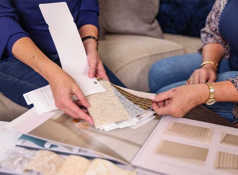 Two women sitting on a couch looking at a book of fabric samples
